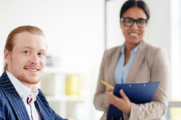 A Businessman sitting at office table with secretary standing takes notes