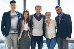A group of 5 professional people standing in a huddle smiling