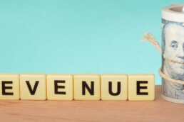 the word revenue spelt out with cash rolled up in a jar
