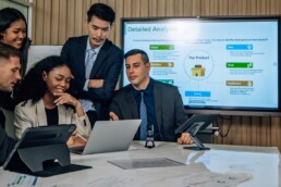 A team of 5 multi racial people gathered around a computer looking at a chart in an office