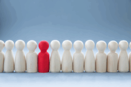 a selection of plain wooded figures in a line with one red one standing out.